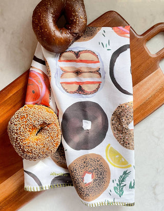 Bagel Tea Towel - Holt x Palm -  Our vibrant tea towels are just the thing to add a touch of colorful flair to your kitchen! Woven from 100% absorbent cotton and printed with our charming, hand-painted designs, each towel is embellished with contrasting embroidery along the seaming. This Tea Towel features whimsical hand-painted donut illustrations in every variety, color, and shape. €¢ 21€³ X 28€³ €¢ HANGING LOOP €¢ EMBROIDERED TRIM €¢ PACKAGED WITH HANGING CARD €¢ MATCHING OVEN MITT + POT HOLDER SET