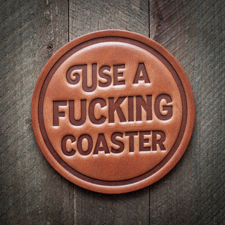 Use a F*cking Coaster Leather Coaster - Holt x Palm -  "Protect your furniture in style with Use a F*cking Coaster Leather Coasters. These funny, passive aggressive coasters make a statement while keeping your surfaces clean. Perfect for anyone with a sense of humor (or a potty mouth!). Don't just protect your furniture, make a statement with Use a F*cking Coaster." Size: 4"